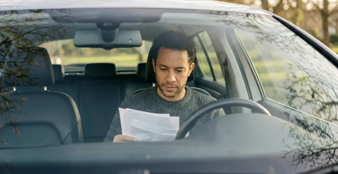Conducteur assis dans un vehicule examine des documents d'assurance